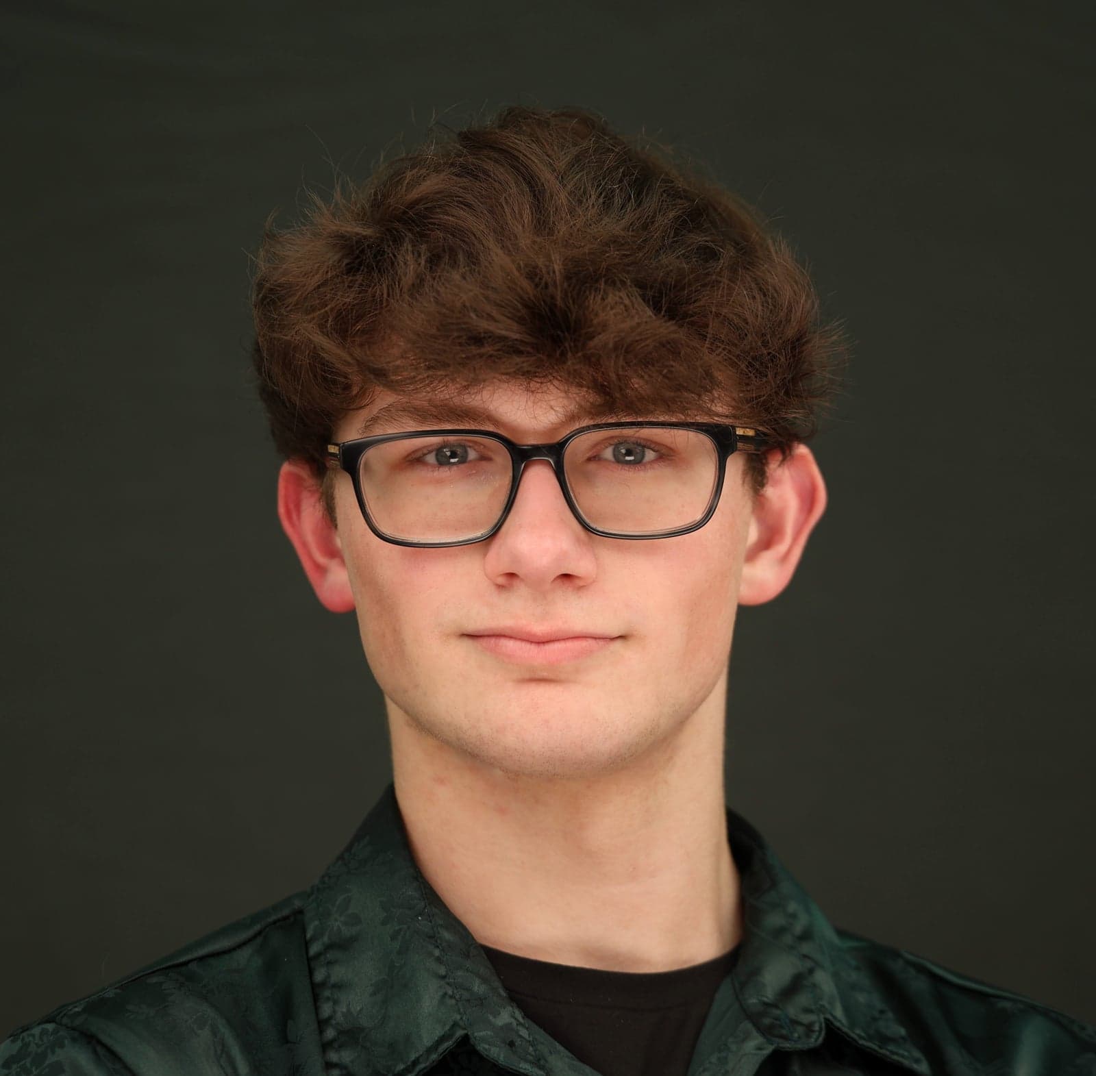 Headshot with glasses and a dark green shirt on a charcoal backdrop